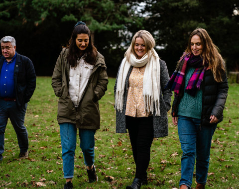 Three women are walking together in conversation with each other. A man is also pictured to the side of them.